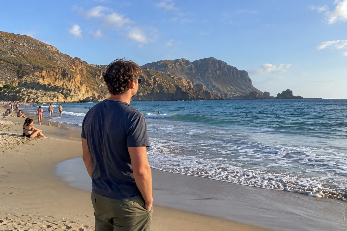 A man looking at the sea on a beach full of tourists — before